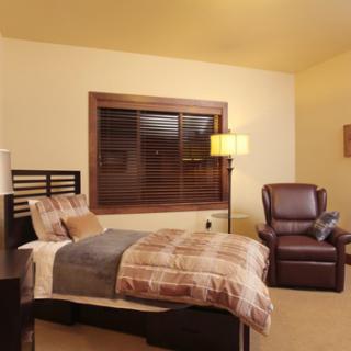 A cozy bedroom with a neatly made bed, an armchair, and a standing lamp next to a window.
