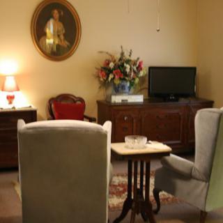 A cozy living room with traditional decor featuring armchairs, a television, and a portrait on the wall.
