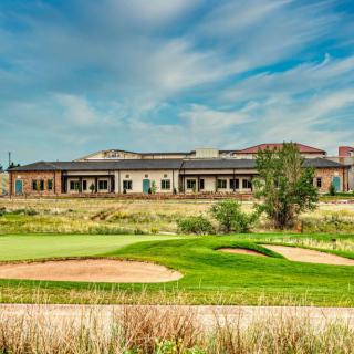 A scenic view of a golf course with a clubhouse in the background under a blue sky.