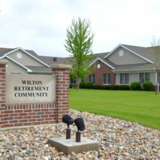 A well-maintained retirement community with a landscaped lawn and a brick sign at the entrance.