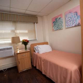 A cozy hospital room with a single bed, nightstand, and colorful artwork on the wall.