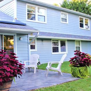 A cozy outdoor patio with chairs and plants in front of a two-story house.