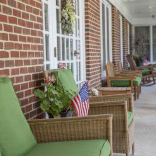 A cozy porch with wicker chairs and green cushions, adorned with plants and American flags.