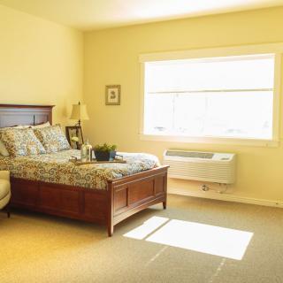 A bright and cozy bedroom with a neatly made bed and ample sunlight streaming through the window.