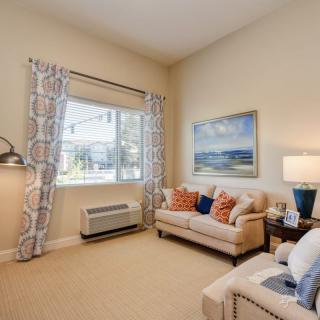 A cozy living room with a sofa, artwork on the wall, and a large window letting in natural light.