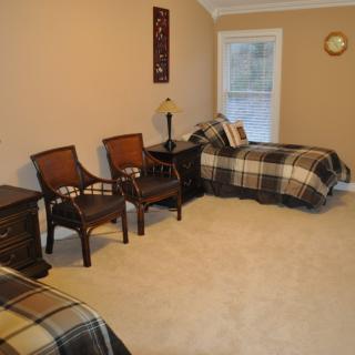 A cozy bedroom with two twin beds featuring checkered bedding, a pair of chairs, and a window allowing natural light.