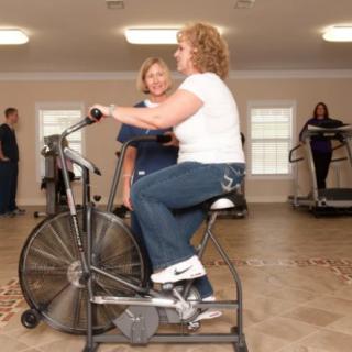 A woman receiving guidance from a trainer while using an exercise bike in a rehabilitation setting.