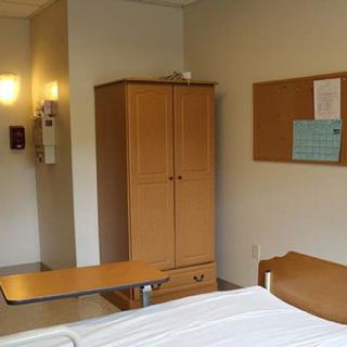 A hospital room with a wardrobe, bedside table, and notice board.