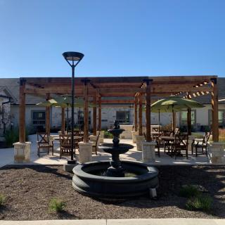 A sunny outdoor seating area with a pergola and a central fountain.