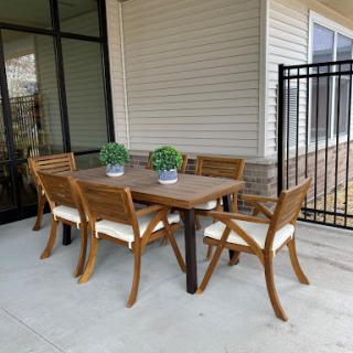 A stylish outdoor dining setup featuring a wooden table and chairs, complemented by potted green plants.