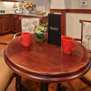 A cozy dining area with a round wooden table set for two, featuring red mugs and a menu.