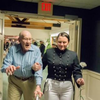 A woman in uniform assisting an elderly man indoors.