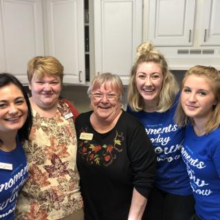 A group of women smiling in a kitchen setting.