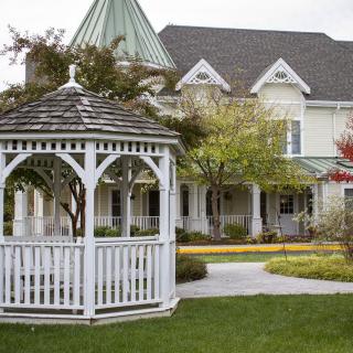 A charming garden scene featuring a white gazebo in front of a spacious house with lush greenery.
