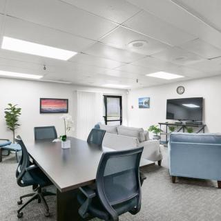 A modern office conference room featuring a large table, chairs, a television, and indoor plants.