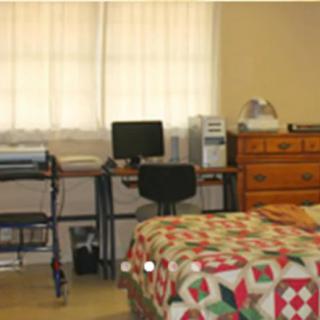A bedroom with a quilted bedspread and a computer desk in the corner.