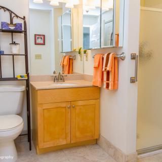 A cozy bathroom with a wooden vanity, mirror, orange towels, and a glass shower.