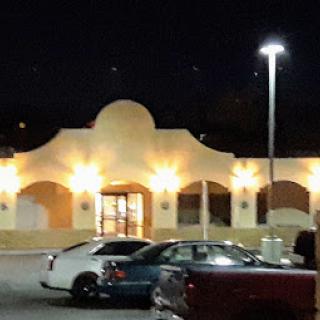A well-lit building at night, surrounded by parked cars.