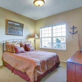 A cozy bedroom with warm tones, featuring a bed with multiple pillows, a window letting in natural light, and nautical decor.