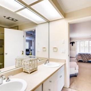 A modern bathroom featuring a double sink vanity with ample lighting and a view into an adjacent room.
