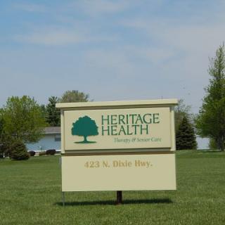 A sign for Heritage Health located outdoors surrounded by grass and trees.