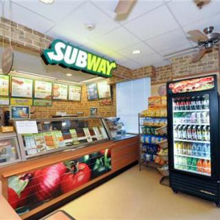 Interior of a Subway restaurant with a counter and beverage cooler.