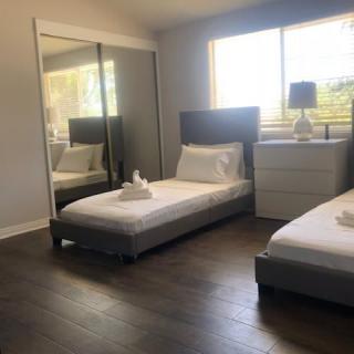 A minimalist bedroom with two twin beds, a large mirrored closet, and a nightstand with a lamp.