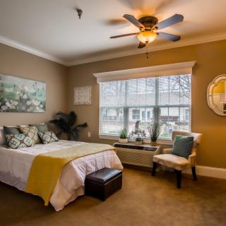 A cozy bedroom with a ceiling fan, artwork on the wall, and a large window allowing natural light to brighten the space.