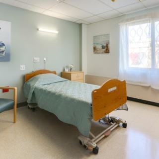 A well-lit and clean hospital patient room featuring a bed, chair, and soft-colored walls.