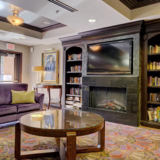 A cozy living room featuring a fireplace, bookshelves, and a television above a modern coffee table.