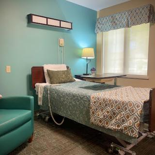 A cozy hospital room featuring a bed, a comfortable chair, and natural light.