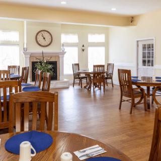 A well-lit dining area featuring wooden tables and chairs, with a fireplace as the focal point.