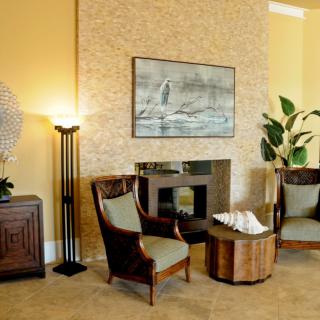 A cozy living room with stylish chairs, a central table, artwork above the fireplace, and decorative plants.
