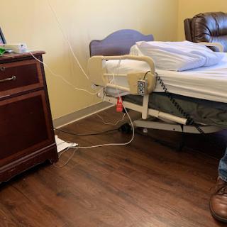 A view of a hospital patient room featuring a bed, wooden furniture, and some medical equipment.