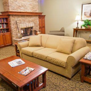 A cozy living room with a beige sofa, a wooden coffee table, a stone fireplace, and bookshelves.