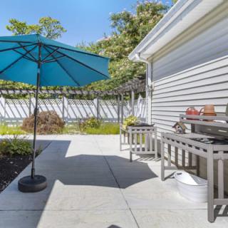 A sunny backyard patio with a blue umbrella and grill.