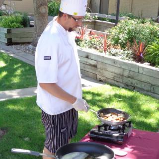 A chef cooking outdoors, wearing a white uniform and hat.