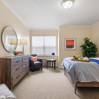 A cozy bedroom with a bed, dresser, and armchair next to a window.