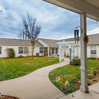 A serene courtyard featuring a winding pathway leading through a manicured garden, surrounded by a building with a welcoming front porch.