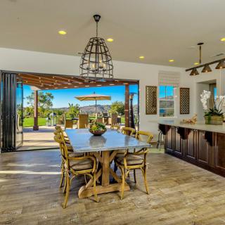 A modern open-plan dining room and kitchen with a seamless transition to an outdoor patio area, featuring wooden flooring and elegant decor.