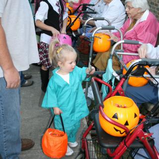 A young child dressed in a Halloween costume collects treats from elderly residents at a nursing home.