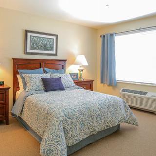 A cozy bedroom with a neatly made bed, wooden furniture, and soft lighting.