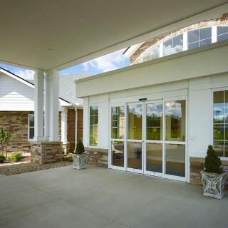 The image shows a building entrance with glass doors, columns, and a covered walkway.
