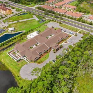 Aerial view of a building complex surrounded by trees and roads, with a nearby water body.