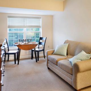 A cozy living room with a sofa, a small dining table, and chairs next to a large window.