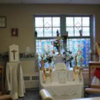 A small Christian altar with a cross, candles, and flowers in front of a stained glass window.