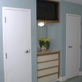 A room with two white doors, a dresser with flowers, and a mounted television.