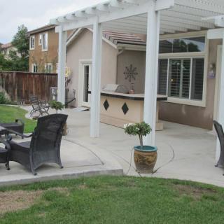 A backyard patio with outdoor furniture and a pergola, adjacent to a house.