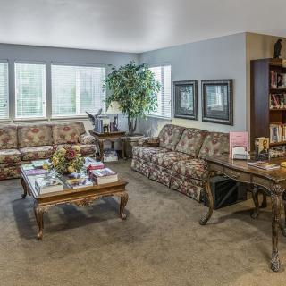 A cozy living room with floral sofas, a central coffee table, and a bookshelf.