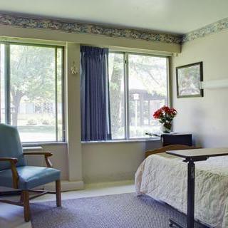 A hospital room with a bed, chair, and window providing natural light.